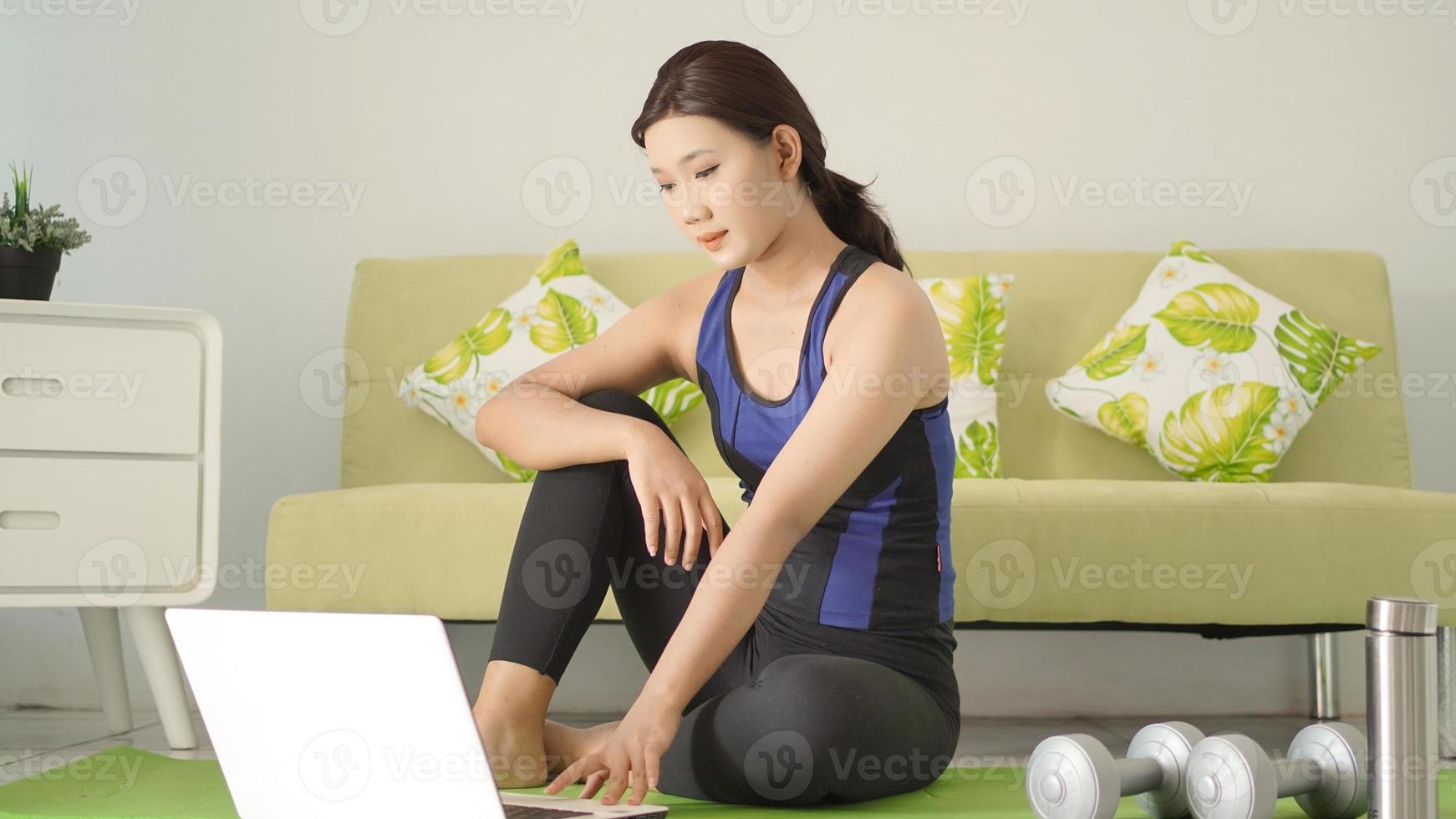 young woman finishes yoga practice looking at laptop screen photo