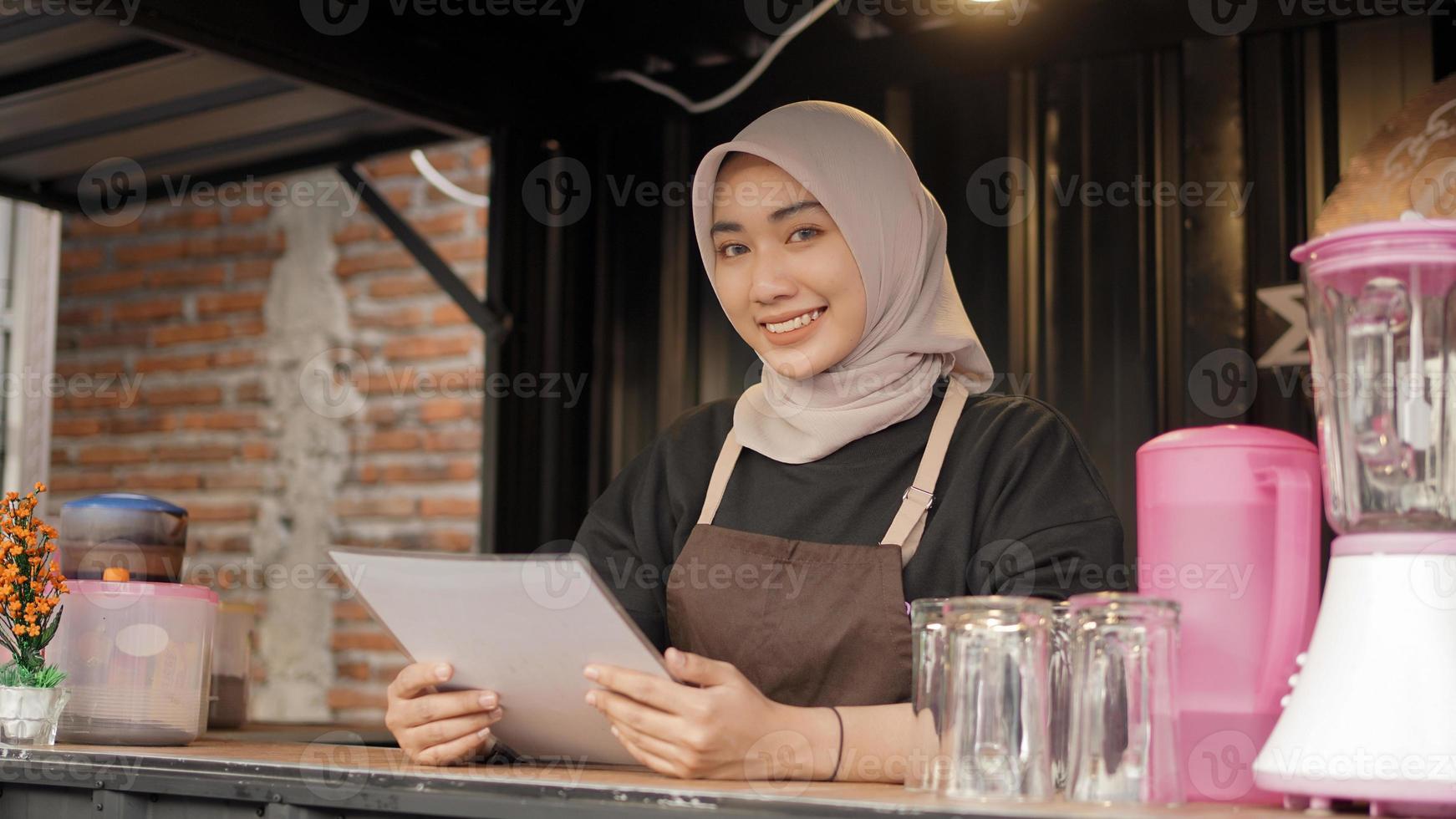 hermosa camarera asiática sonriente que lleva la lista del menú en el contenedor de la cabina del café foto