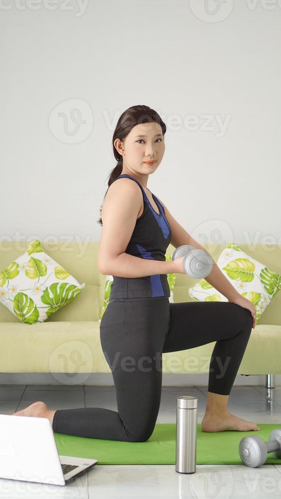 asian woman lifting half-arm barbell while squatting at home photo