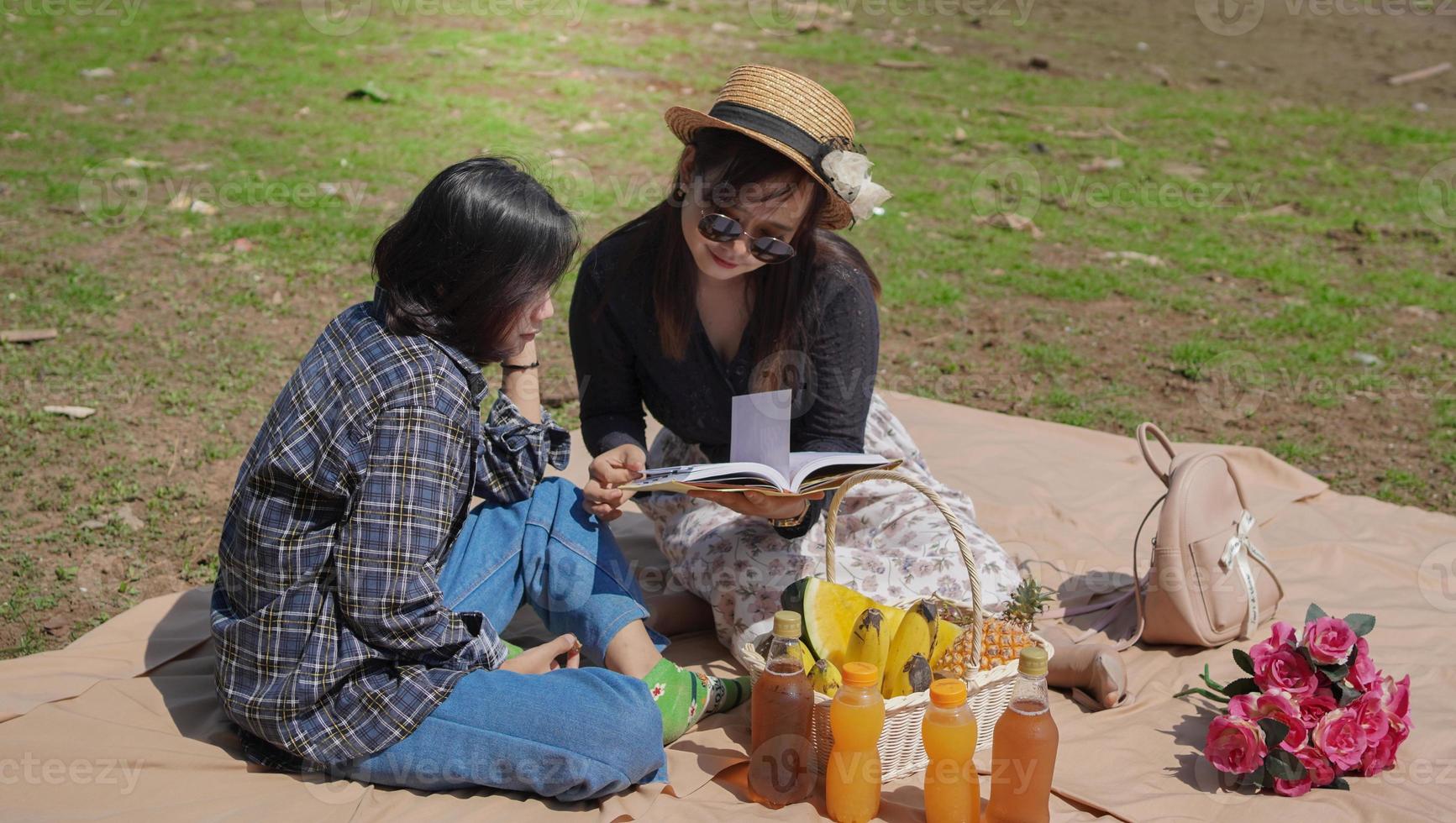 two happy young asian women reading a book while vacationing by the lake photo