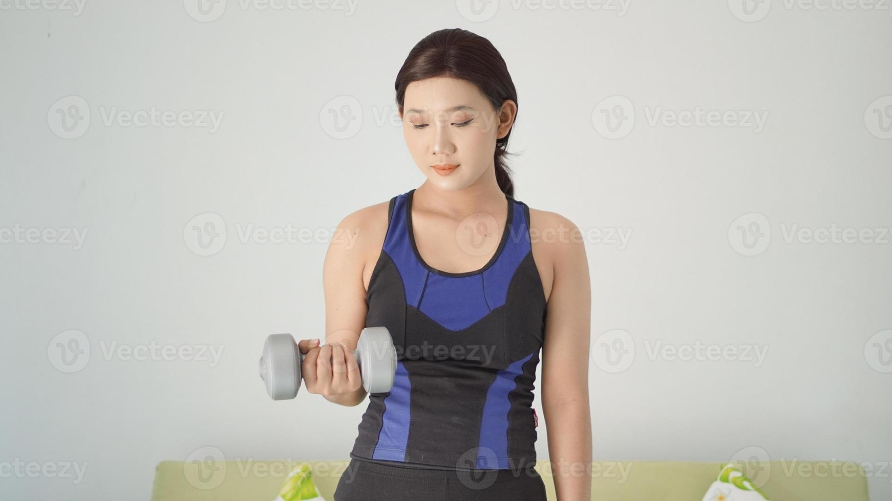 asian woman lifting half-arm barbell while standing at home photo
