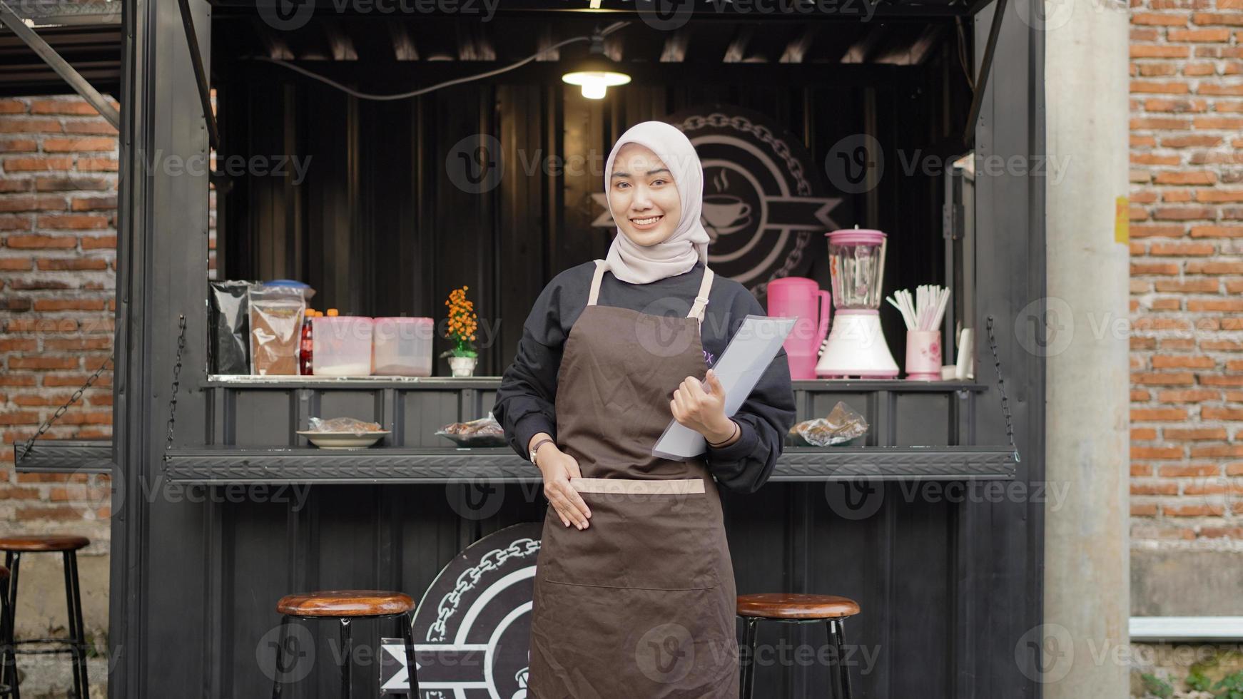 hermosa camarera asiática trae una lista de menús listos para abrir en el contenedor de la cabina del café foto