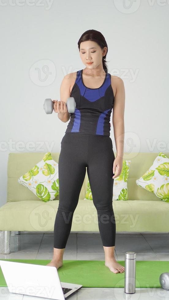 asian woman lifting half-arm barbell while standing at home photo