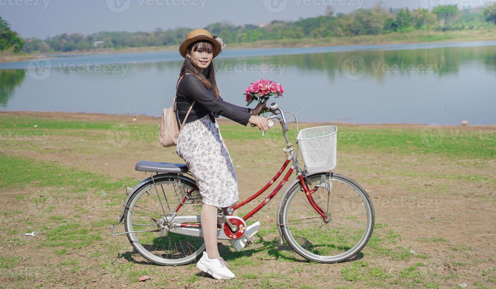 joven asiática disfrutando del ciclismo sosteniendo flores en el parque foto