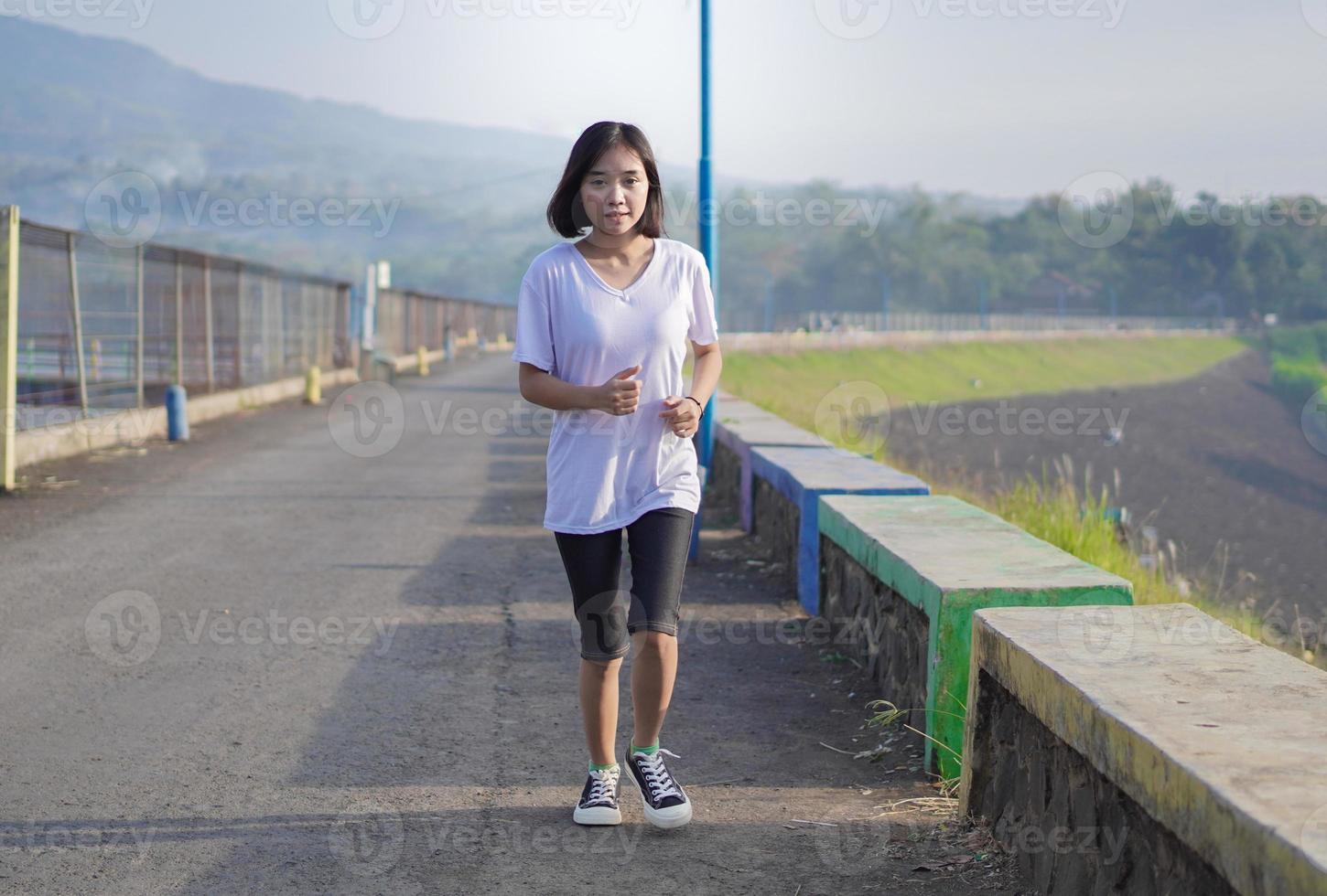 Young fitness Asian woman is running and jogging an outdoor workout on the road in the morning photo