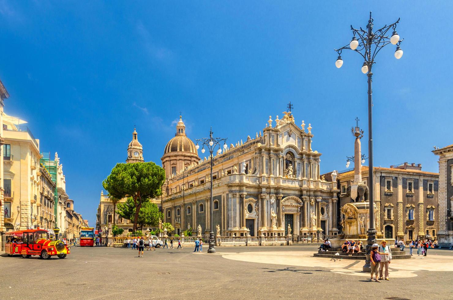 italia, catania, 13 de mayo de 2018 fuente de estatua de elefante, catedral de santa agatha, tren rojo turístico y gente caminando en la plaza piazza del duomo en catania foto