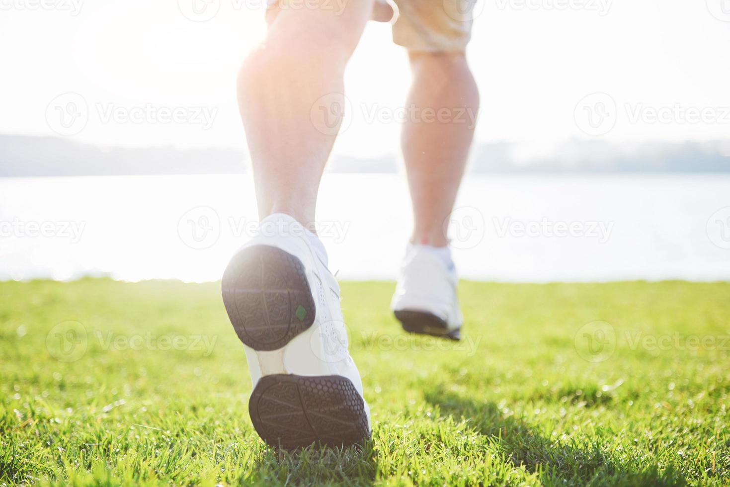 Outdoor cross-country running in summer sunshine concept for exercising, fitness and healthy lifestyle. Close up of feet of a man running in grass photo