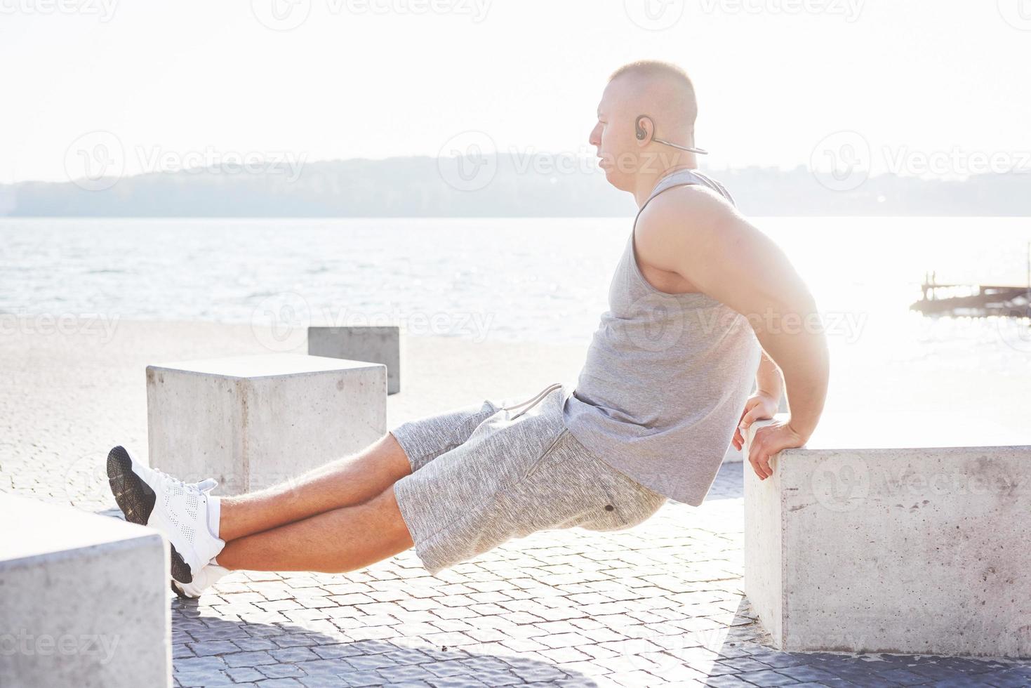Profile view of a strong man exercising his arms and doing tricep dips outdoors in a park bench photo