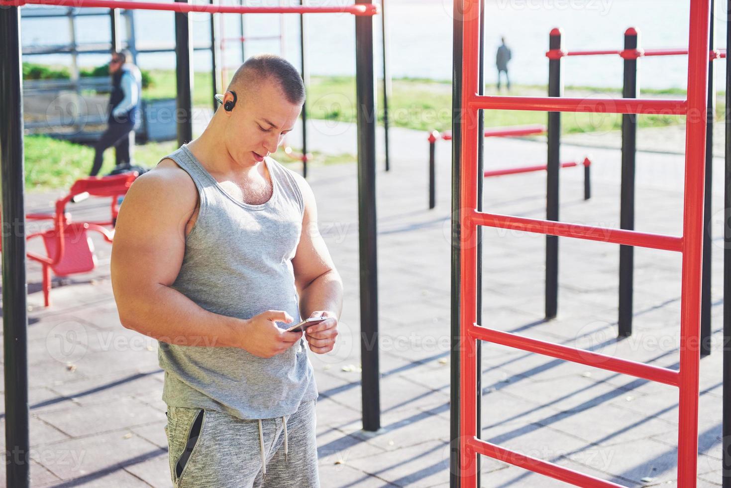 hombre musculoso con hermoso torso haciendo ejercicio en barras horizontales sobre un fondo borroso del parque. joven haciendo pull-ups al aire libre foto