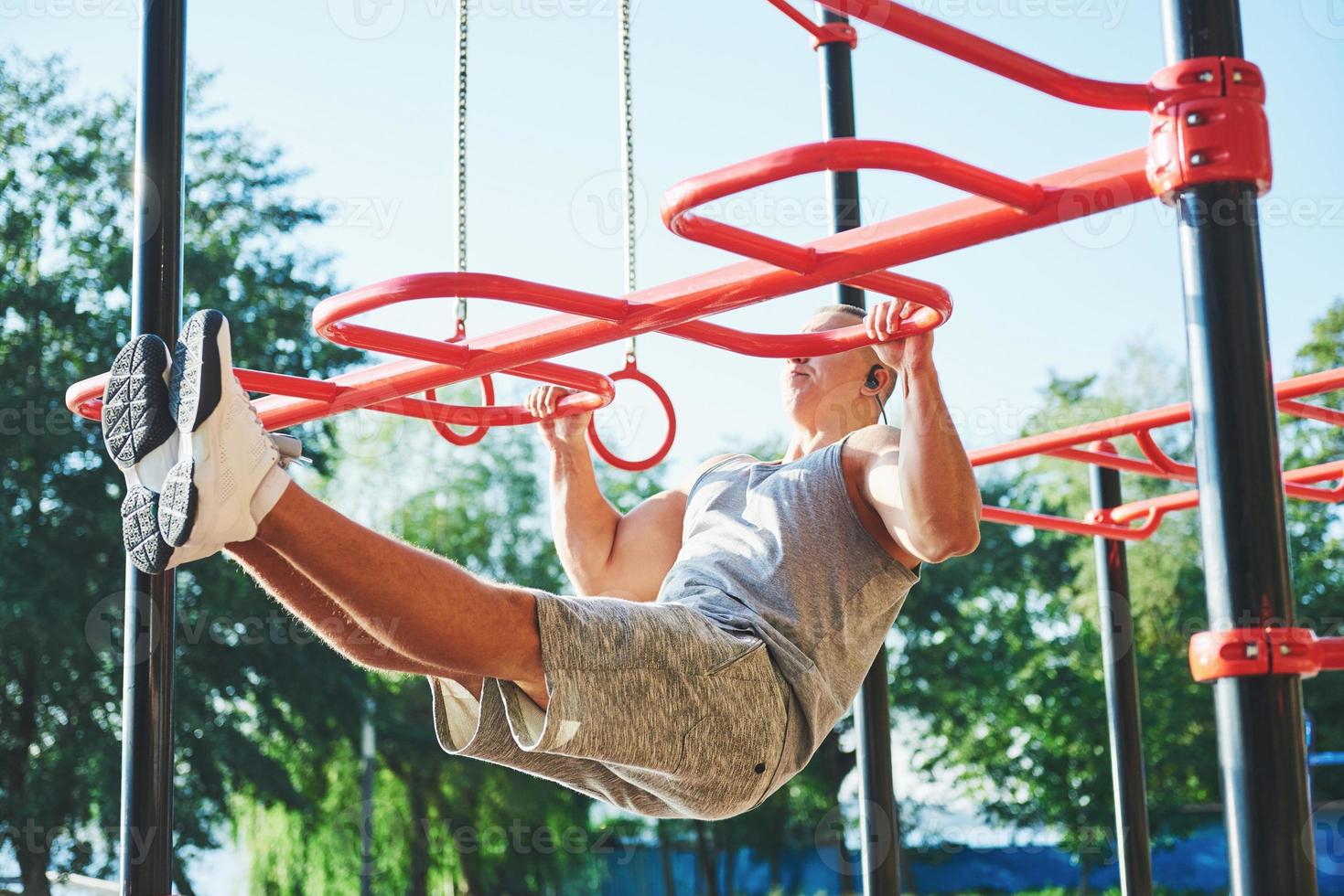 Muscular man with beautiful torso exercising on horizontal bars on a blurred park background. Young man doing pull-ups outdoors photo