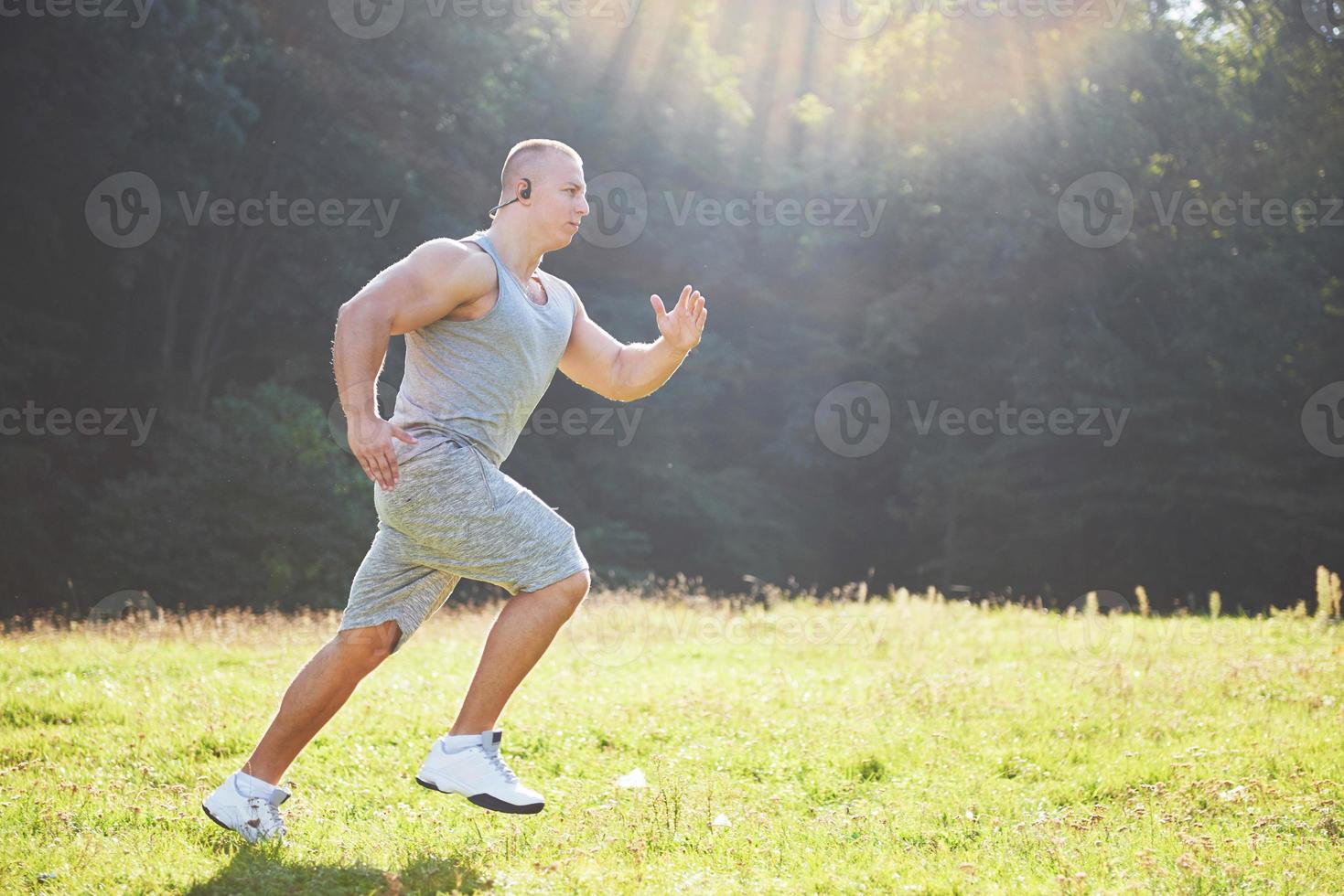 atleta fitness hombre trotando en la naturaleza durante la puesta de sol. persona corriendo ejercitándose viviendo un estilo de vida activo entrenando cardio en verano en ropa deportiva y zapatos. foto