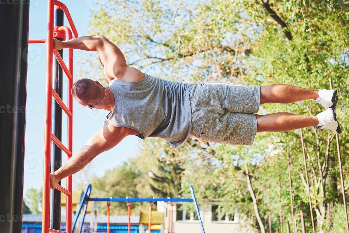 Muscular man with beautiful torso exercising on horizontal bars on a blurred park background. Young man doing pull-ups outdoors photo