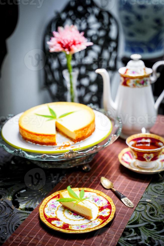 Cheesecake dessert pie, dairy recipe homemade on table. Delicious fresh peace of cake slice on plate. Tasty sweet food cannabis leaves on top. Morning gourmet plate closeup dish photography. photo