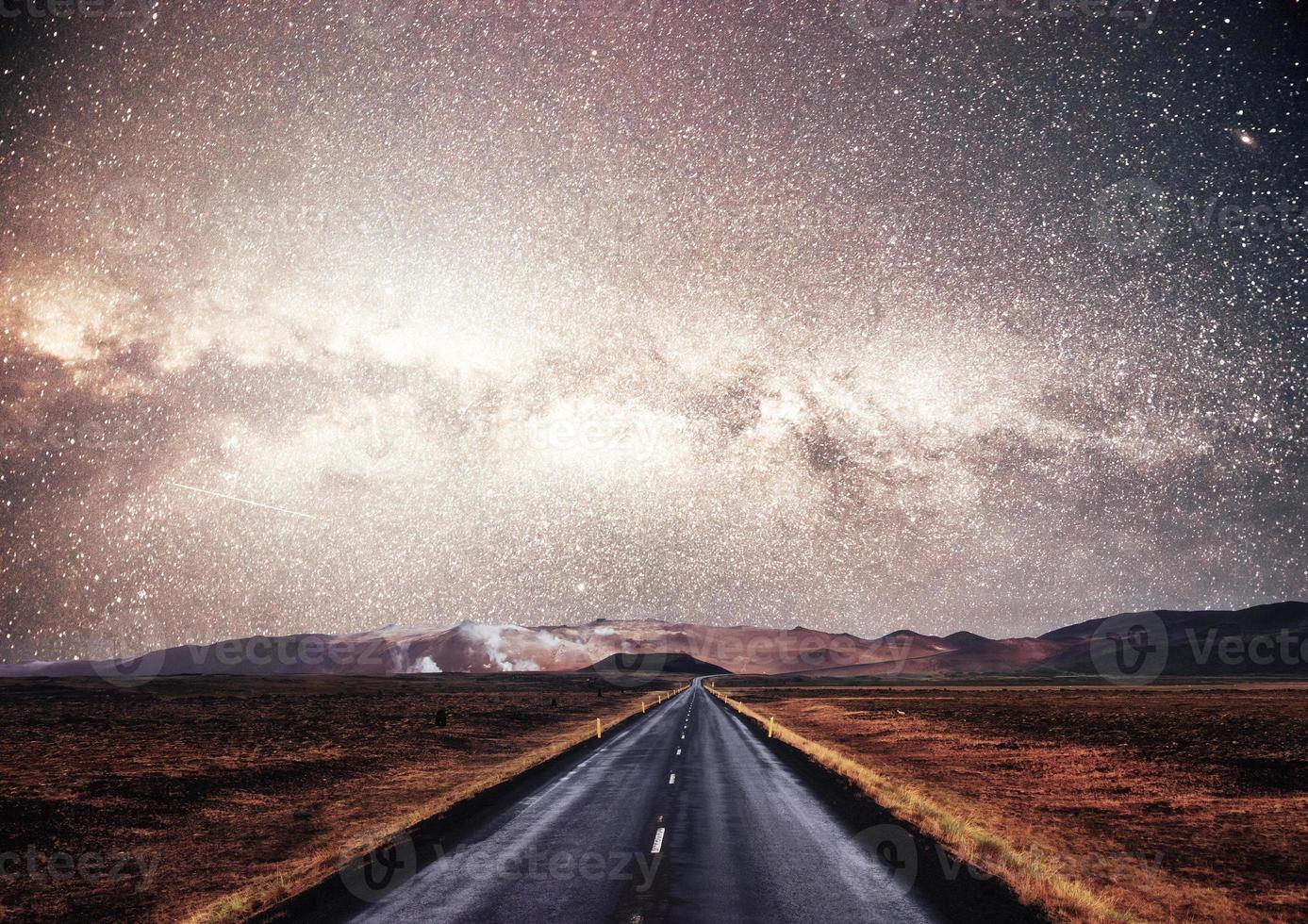 Starry Sky over the mountains. The asphalt road with white markings. Beautiful summer landscape. Soft filtering effect. Iceland photo