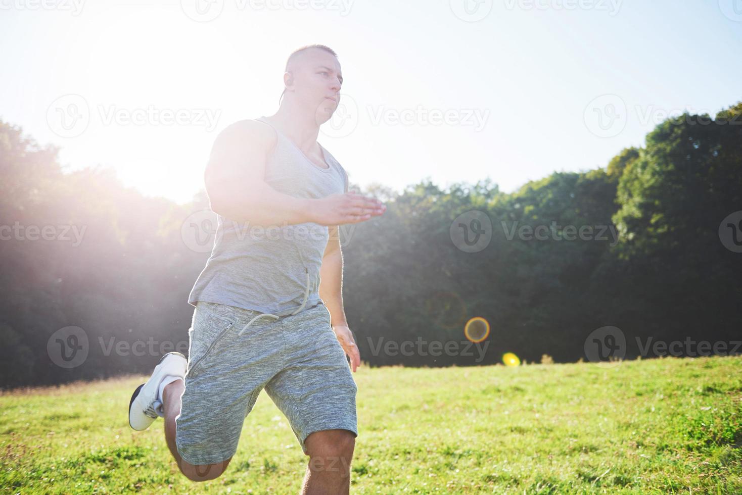 atleta fitness hombre trotando en la naturaleza durante la puesta de sol. persona corriendo ejercitándose viviendo un estilo de vida activo entrenando cardio en verano en ropa deportiva y zapatos. foto