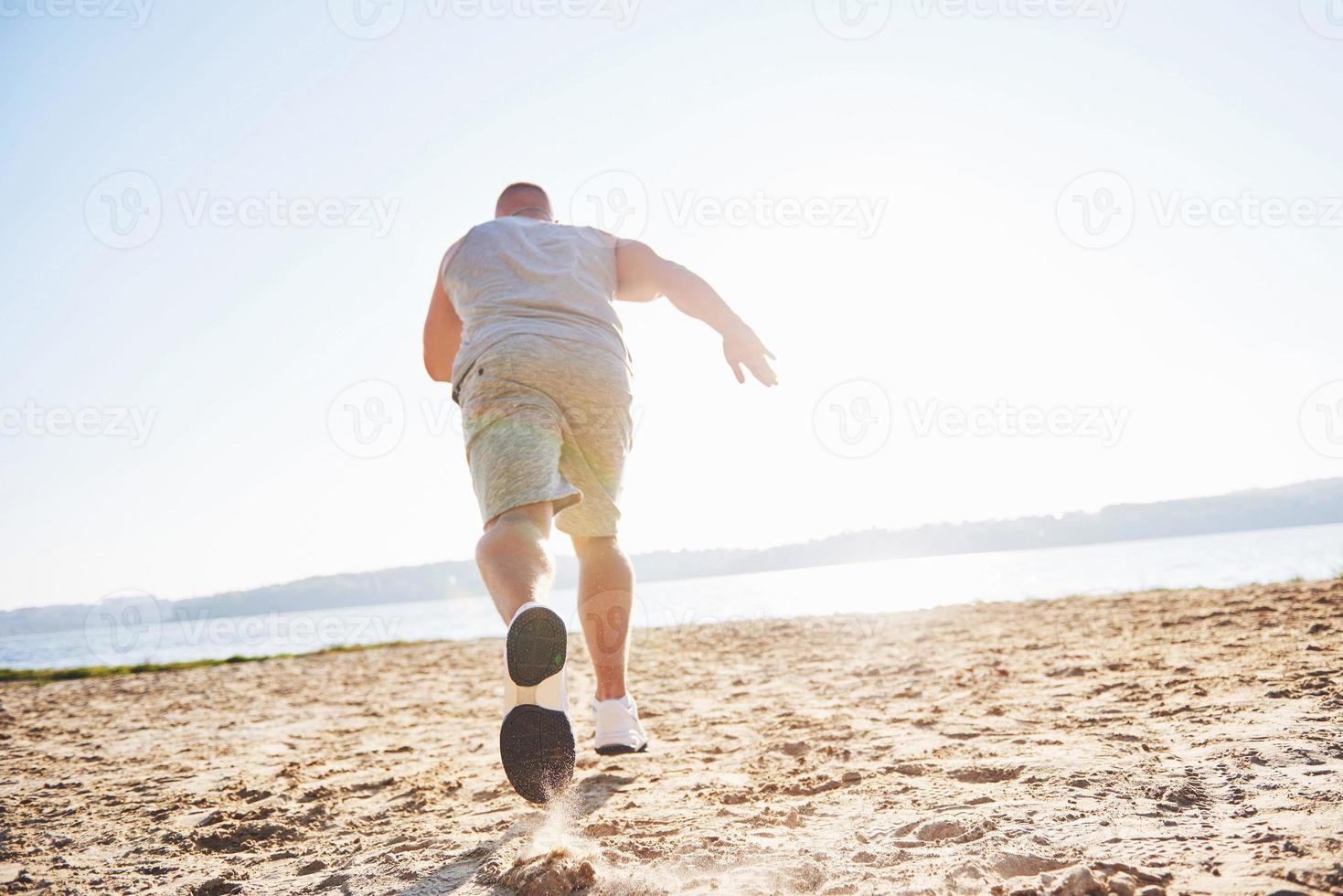 A athletic man looking at the seaside on the wild sand beach. Masculine and sporty male with naked torso is doing evening training at the sea cost. Summer work-out training outdoors photo