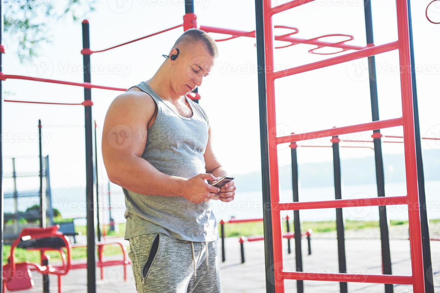 Muscular man with beautiful torso exercising on horizontal bars on a blurred park background. Young man doing pull-ups outdoors photo