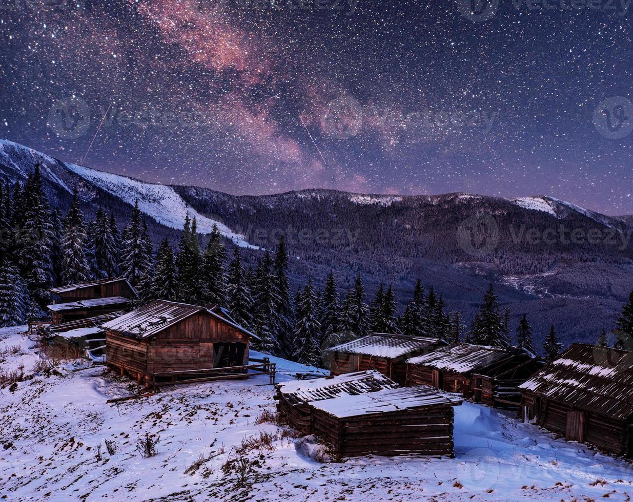 magical winter snow covered trees and mountain village. Winter landscape. Vibrant night sky with stars and nebula and galaxy. photo