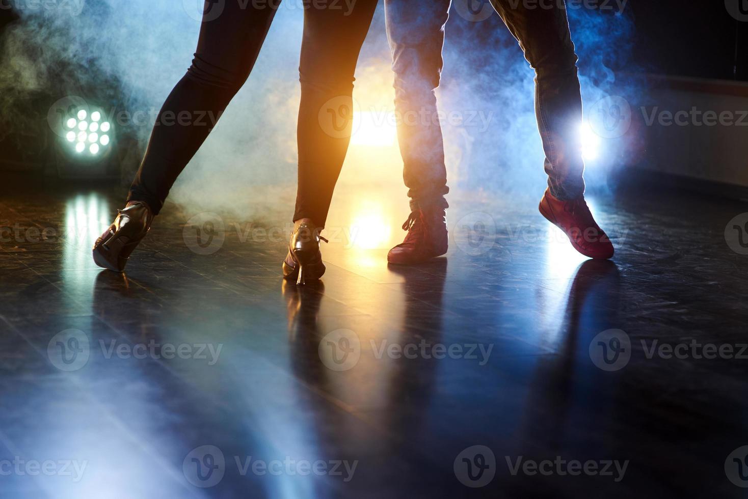 hábiles bailarines actuando en el cuarto oscuro bajo la luz y el humo del concierto. hermosas piernas femeninas y masculinas en danza activa foto