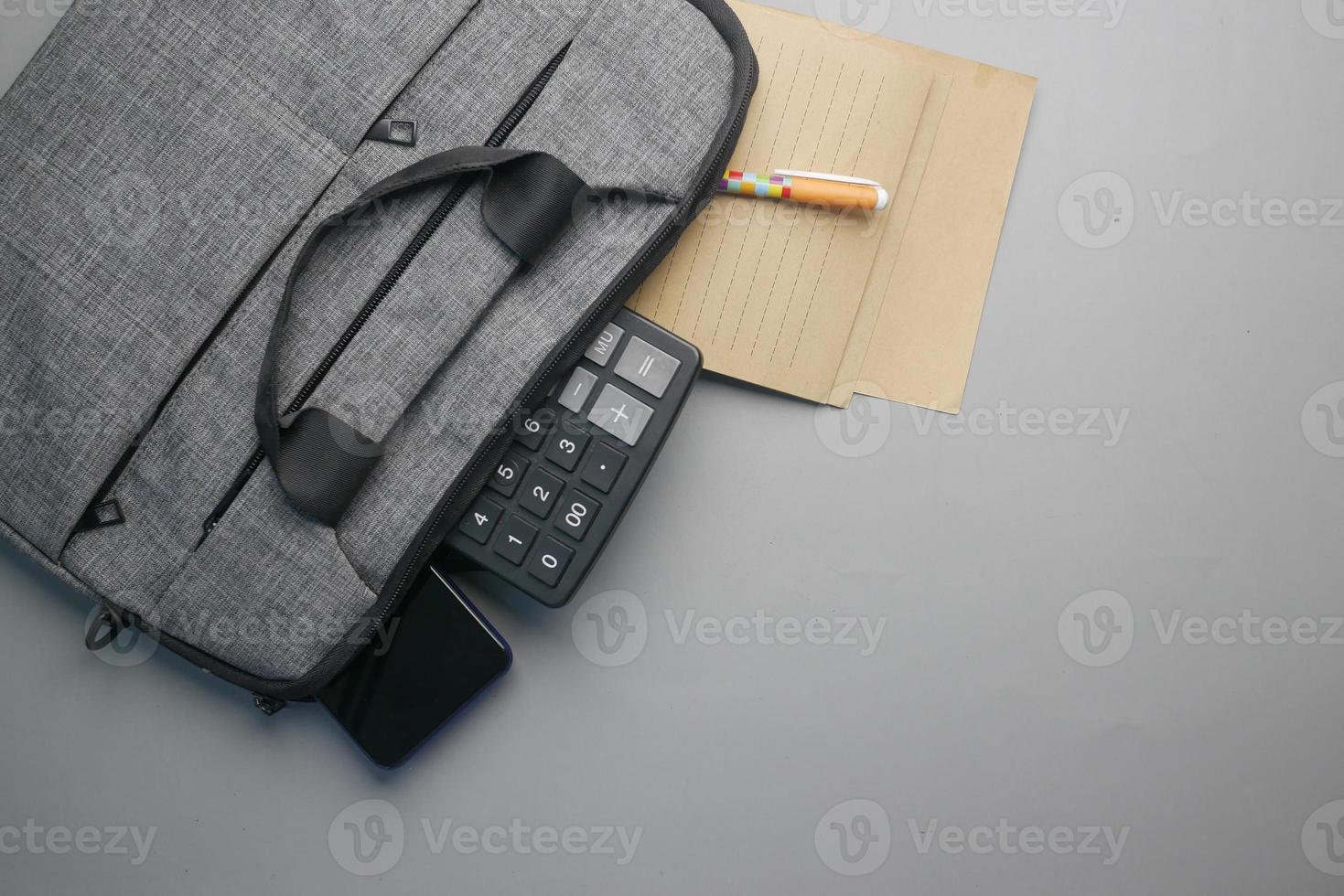 Top view of note pad, calculator, pen in a office bag on gray background photo