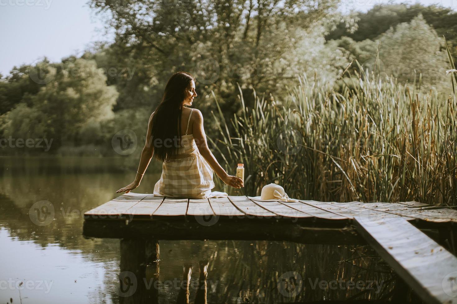 Young woman relaxing on the wooden pier at the calm lake photo