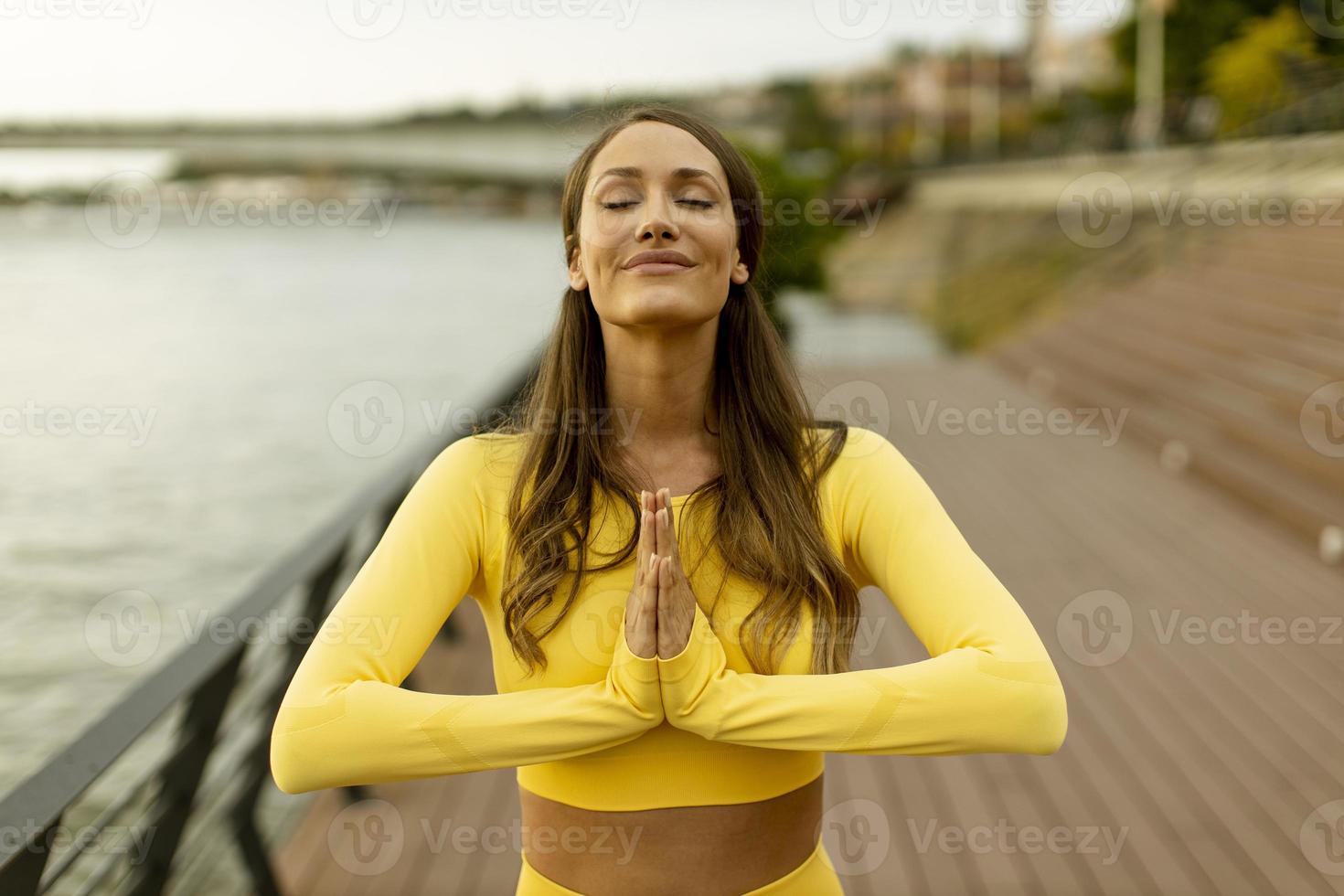 Young woman having stretching exercise on the riverside pier photo