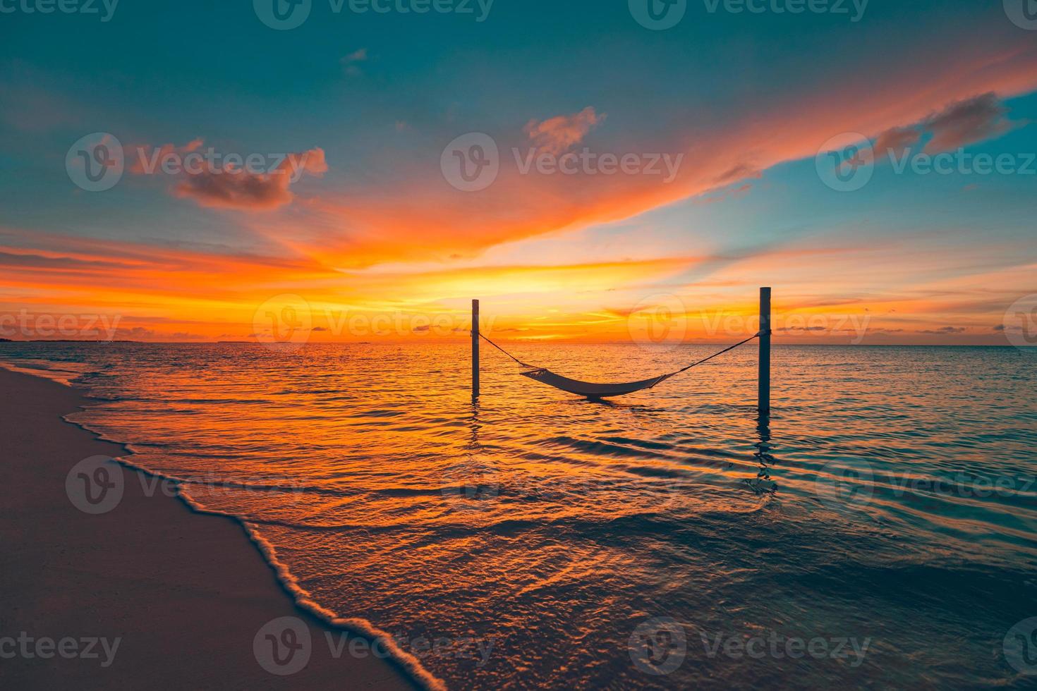 Tropical sunset beach as summer landscape panorama with beach swing or hammock. Colorful sky, sand palm tree leaves and calm sea beach banner. Couple romantic beach scene photo