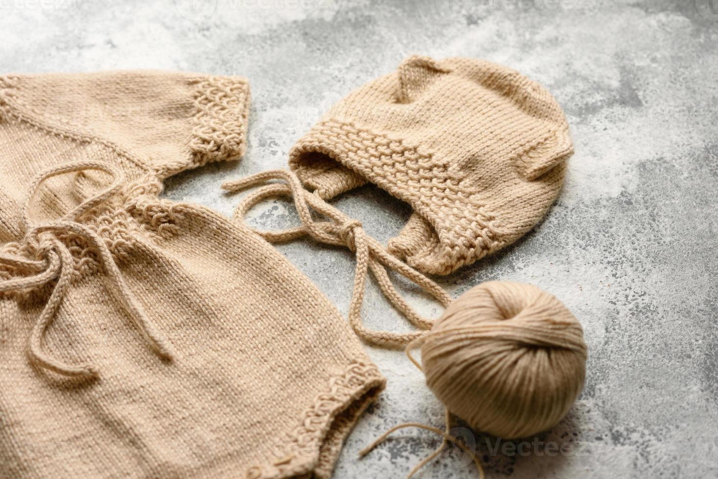 Baby knitted beige clothes on a white concrete background photo
