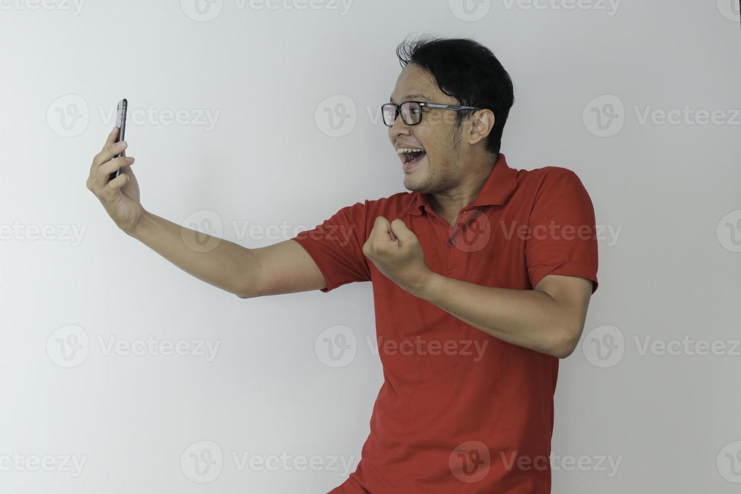 Young Asian man shocked and happy with what he see in the smartphone on isolated grey background. photo