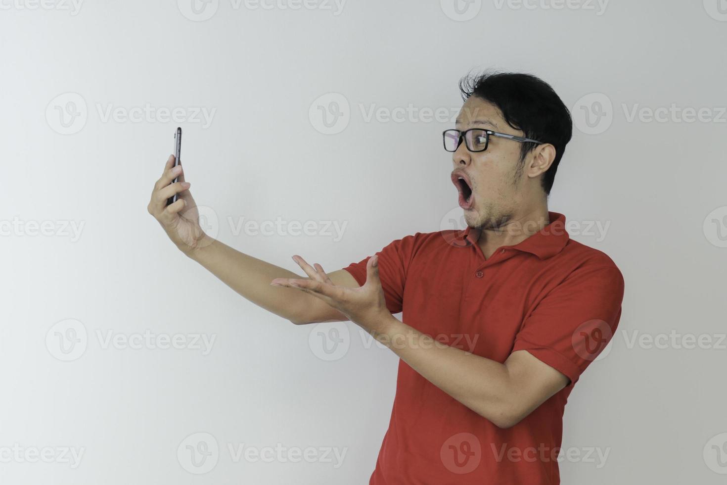 wow, la cara de un joven asiático se sorprendió por lo que vio en el teléfono inteligente con un fondo gris aislado. foto