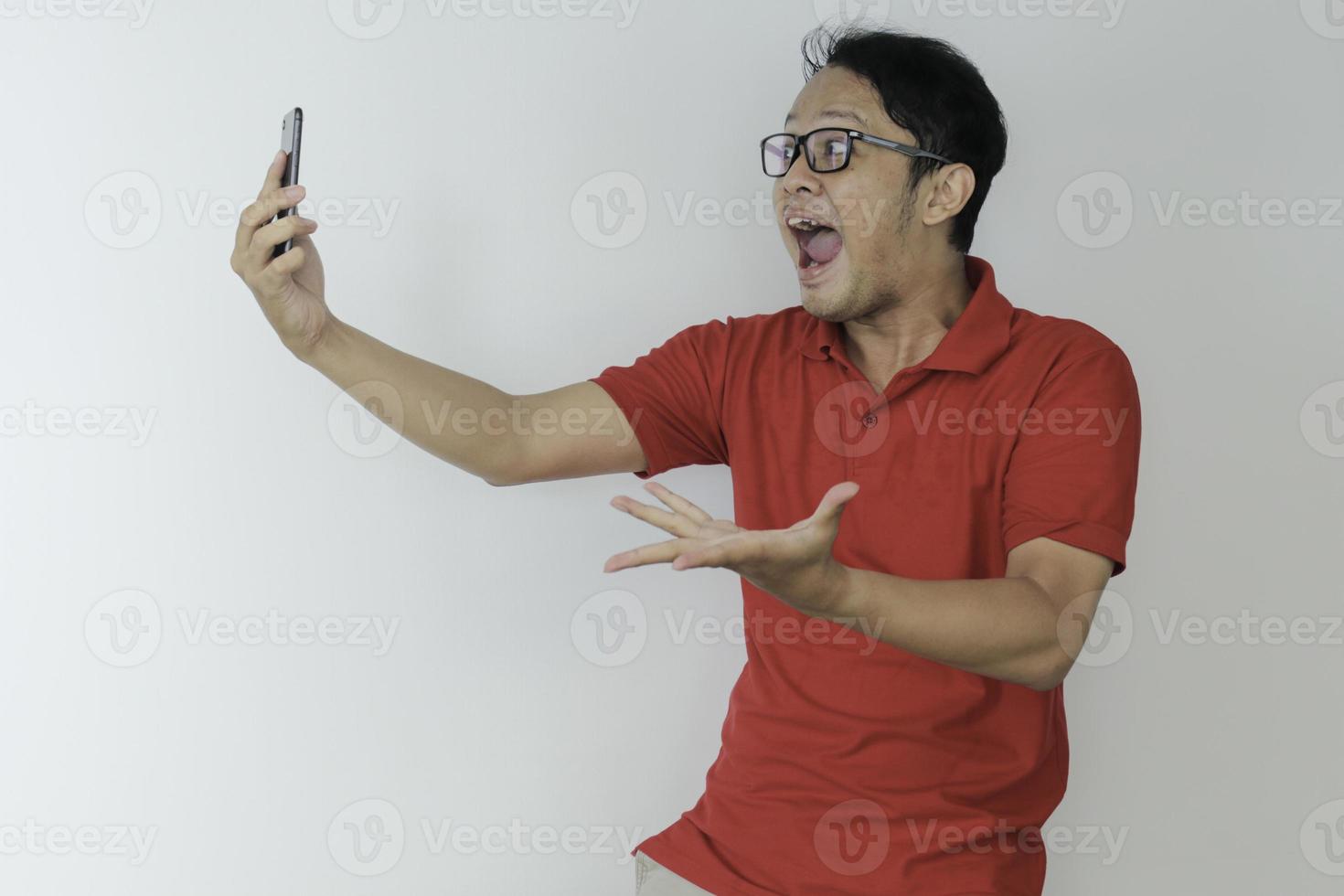 Young Asian man shocked and happy with what he see in the smartphone on isolated grey background. photo