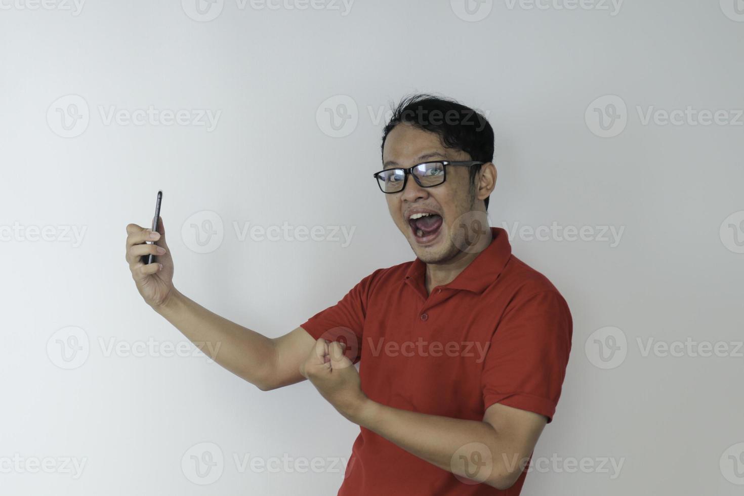 Young Asian man shocked and happy with what he see in the smartphone on isolated grey background. photo