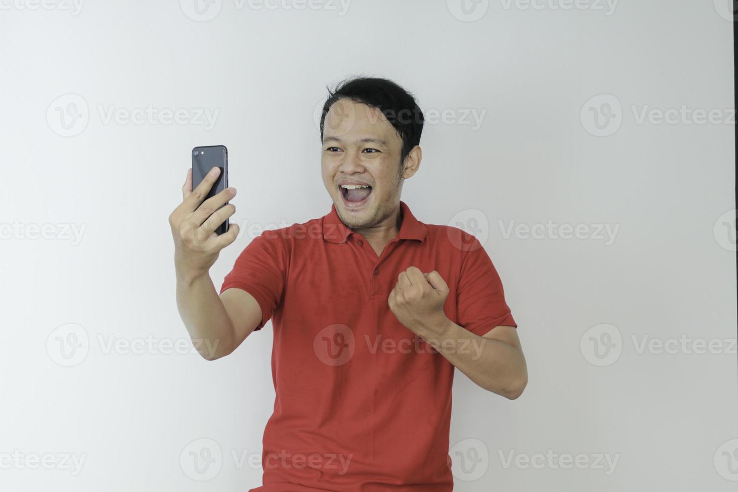 Young Asian man shocked and happy with what he see in the smartphone on isolated grey background. photo