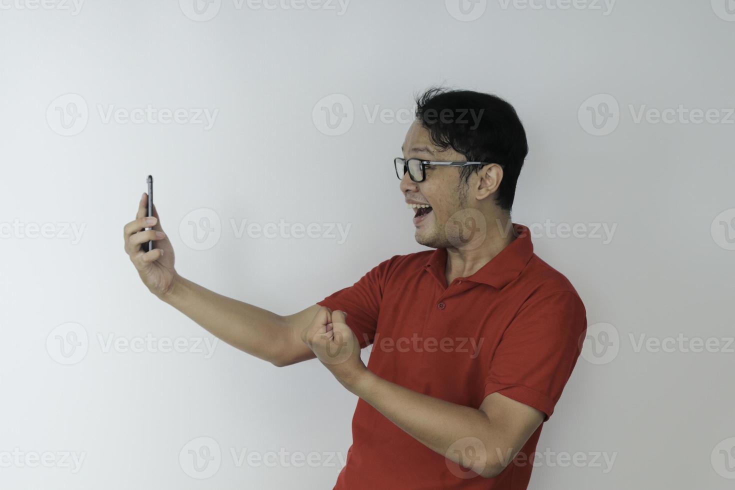 joven asiático conmocionado y feliz con lo que ve en el teléfono inteligente en un fondo gris aislado. foto