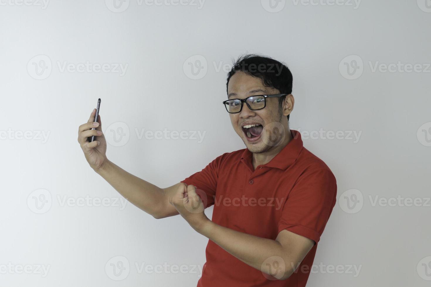 Young Asian man shocked and happy with what he see in the smartphone on isolated grey background. photo