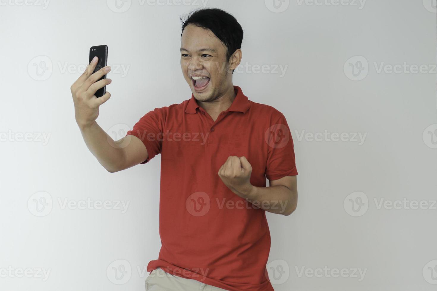 Young Asian man shocked and happy with what he see in the smartphone on isolated grey background. photo