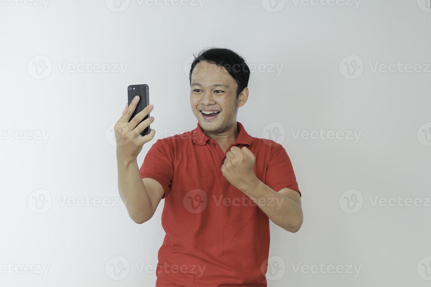 Young Asian man shocked and happy with what he see in the smartphone on isolated grey background. photo