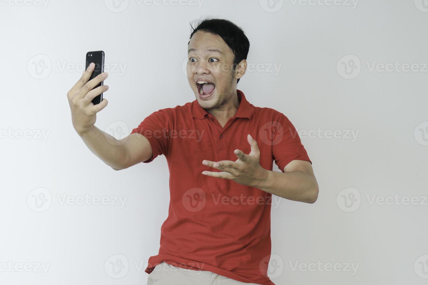 Young Asian man shocked and happy with what he see in the smartphone on isolated grey background. photo