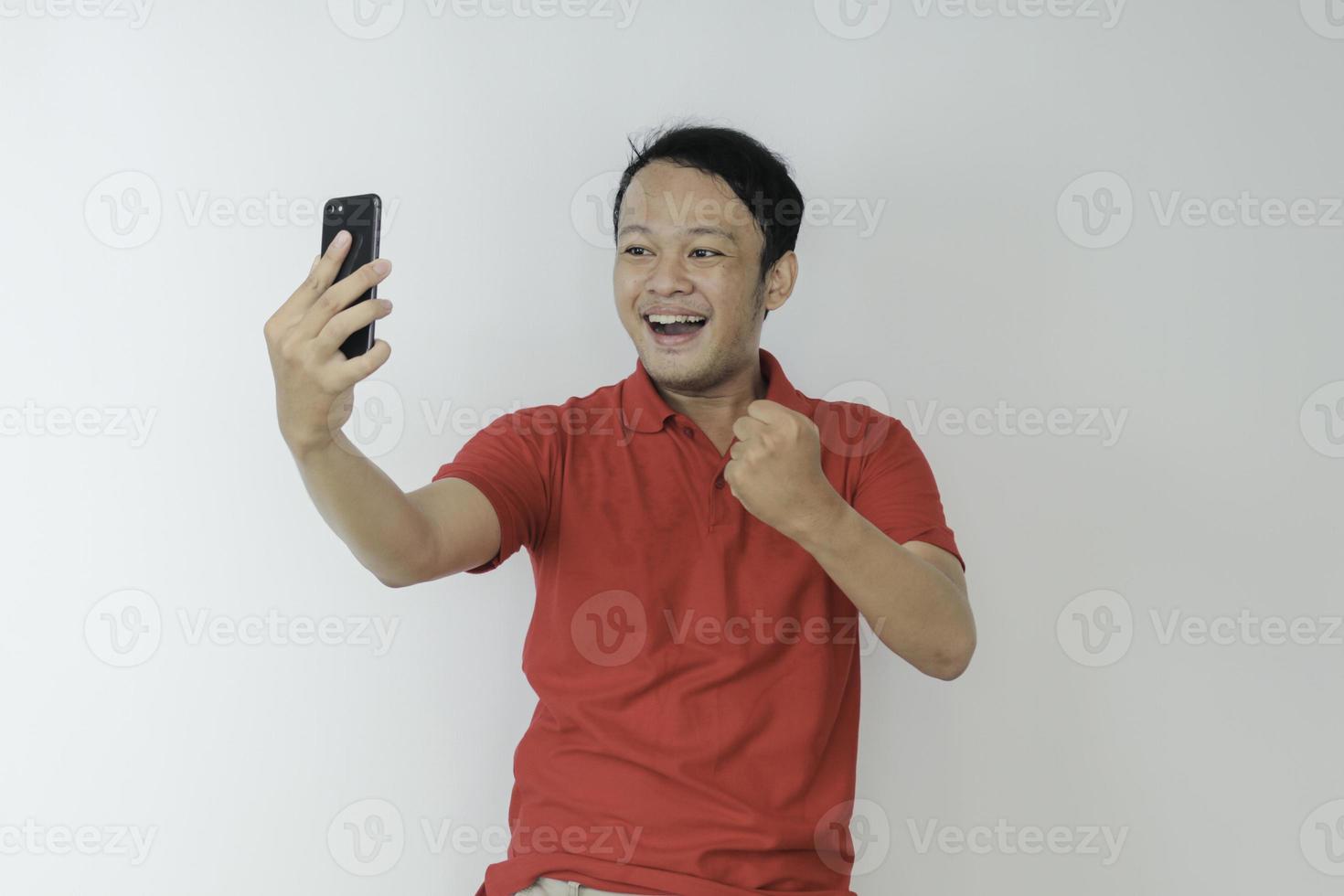 Young Asian man shocked and happy with what he see in the smartphone on isolated grey background. photo