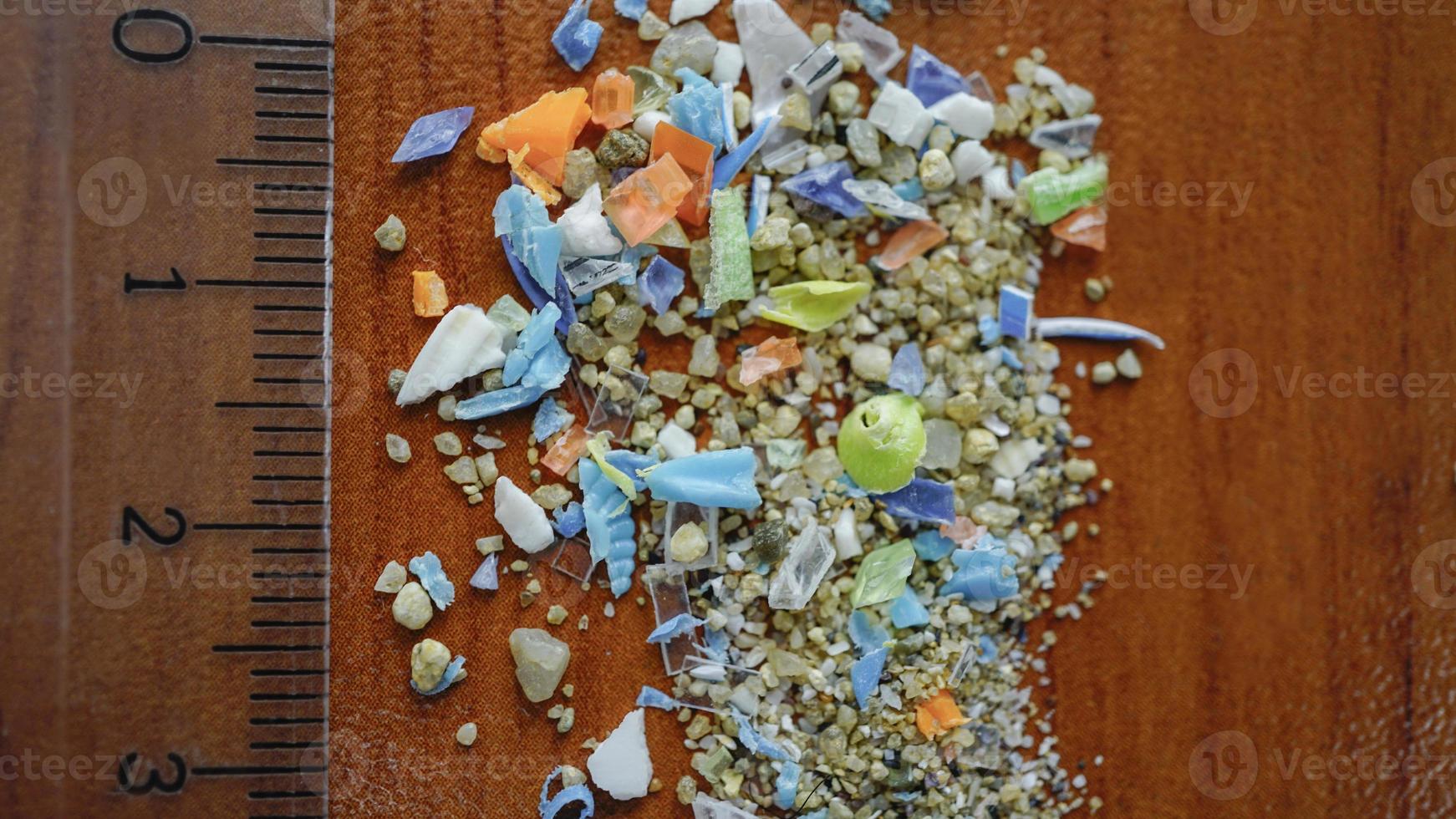 Macro shot of authentic real microplastic particles gathered from the beach with a ruler to show their size. Water pollution and global warming concept. photo