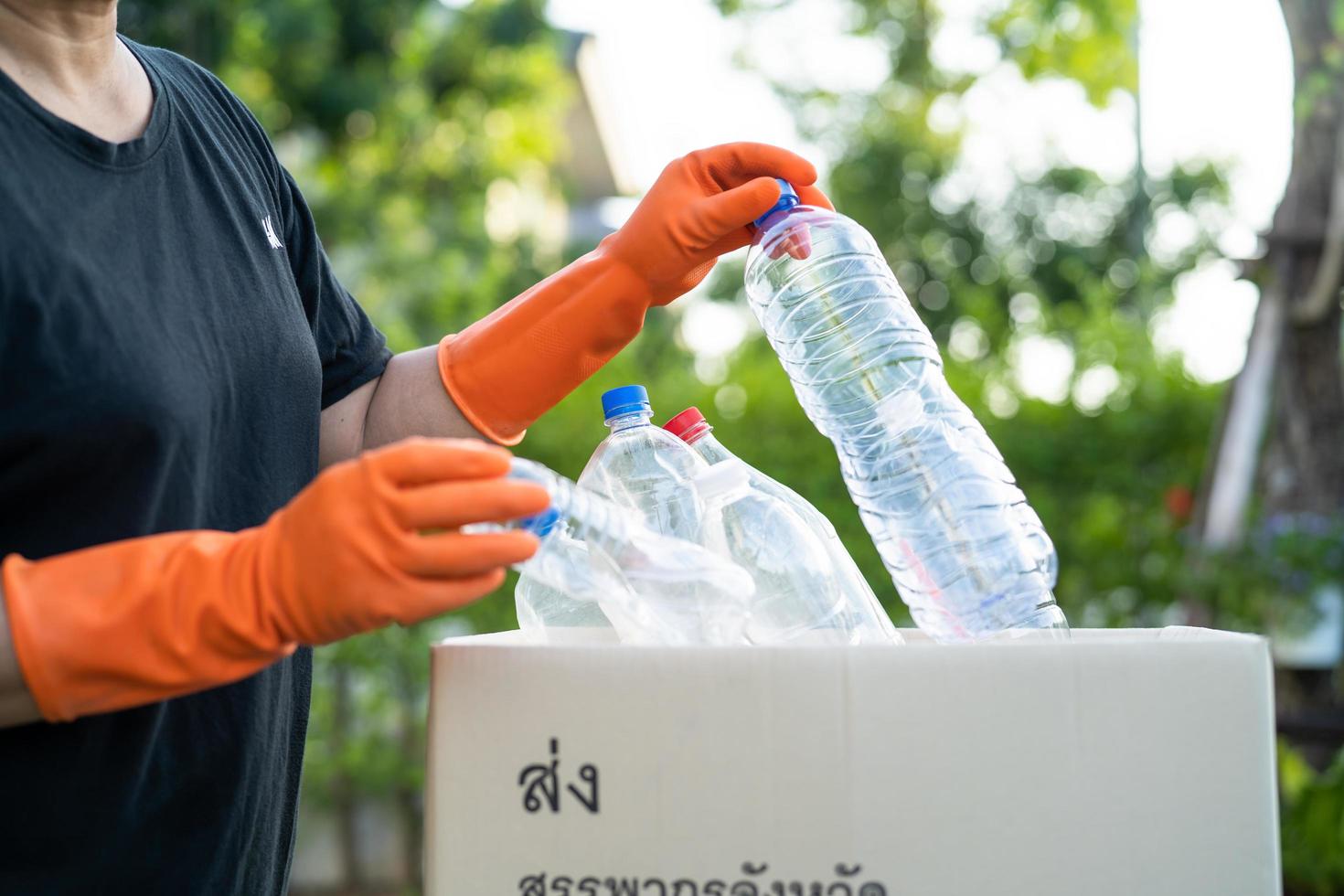 Asian woman volunteer carry water plastic bottles into garbage box trash in park, recycle waste environment ecology concept. photo