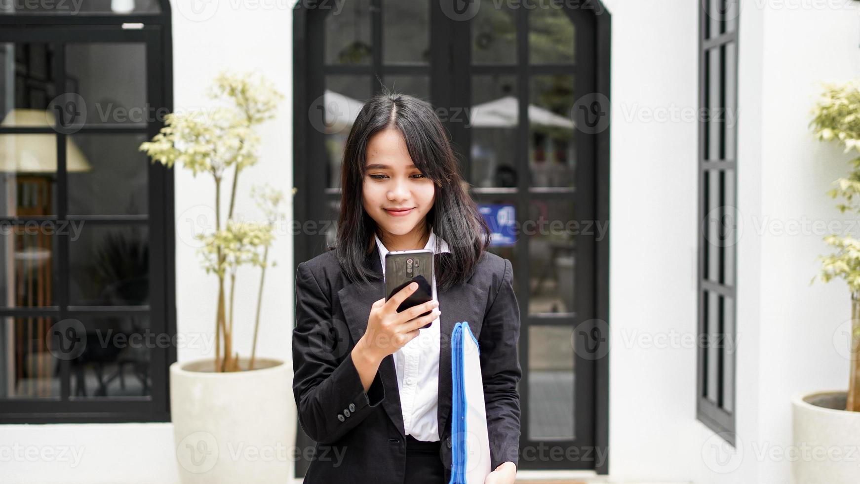 hermosa joven mujer de negocios asiática en traje de pie en el café con teléfono y sobre marrón foto