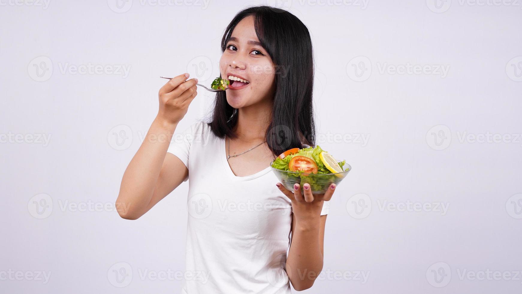 joven mujer asiática feliz comiendo ensalada saludable con fondo blanco aislado foto