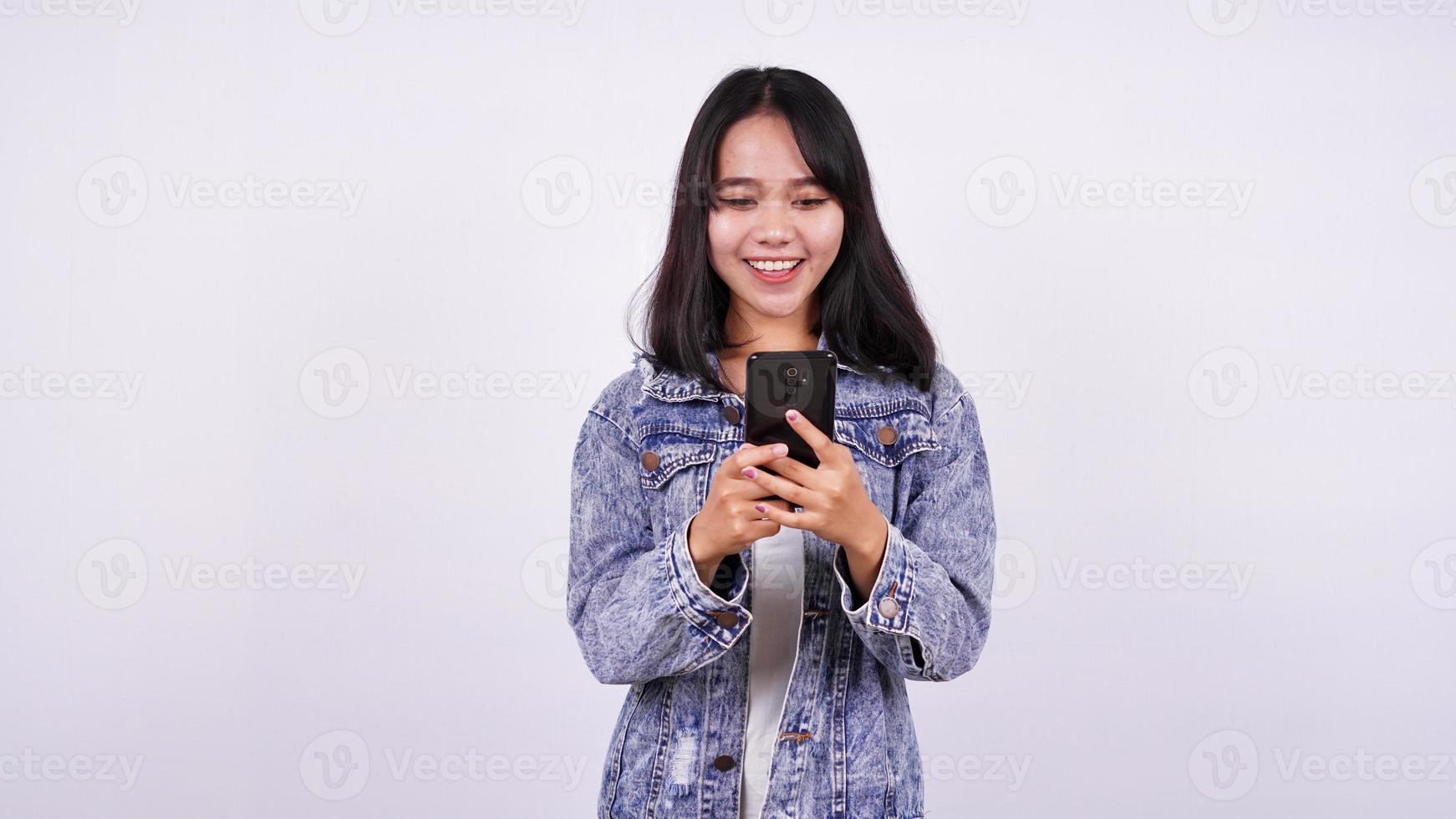 mujeres asiáticas sonriendo con una chaqueta de jeans y sosteniendo un teléfono con un fondo blanco aislado foto