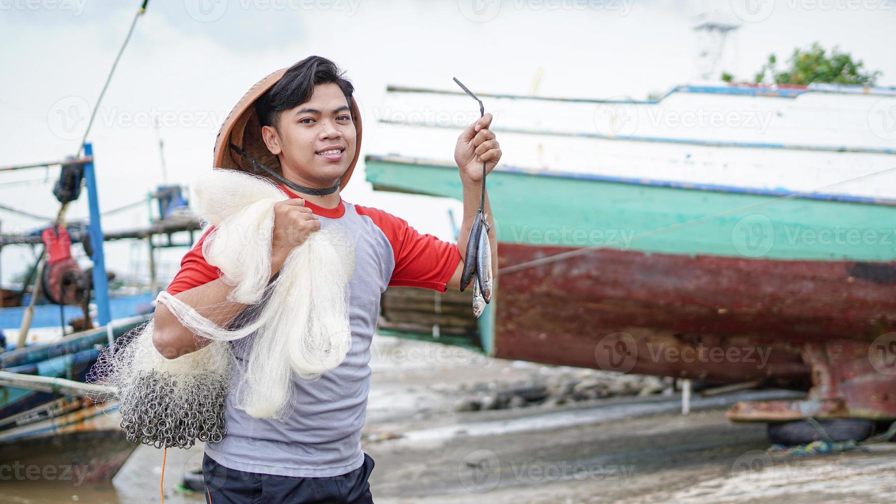 Happy young fisherman on the beach holding his catch fish and shows in front of his boat photo