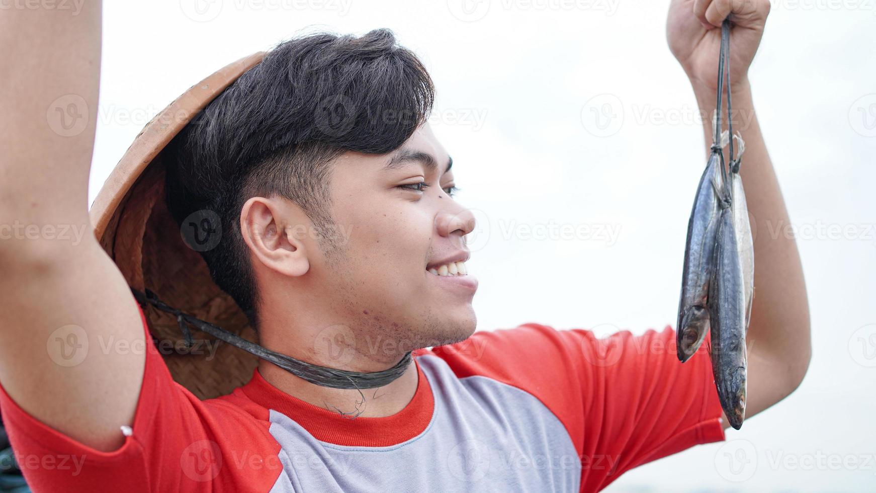 Happy young fisherman on the beach holding his catch fish and shows in front of his boat photo