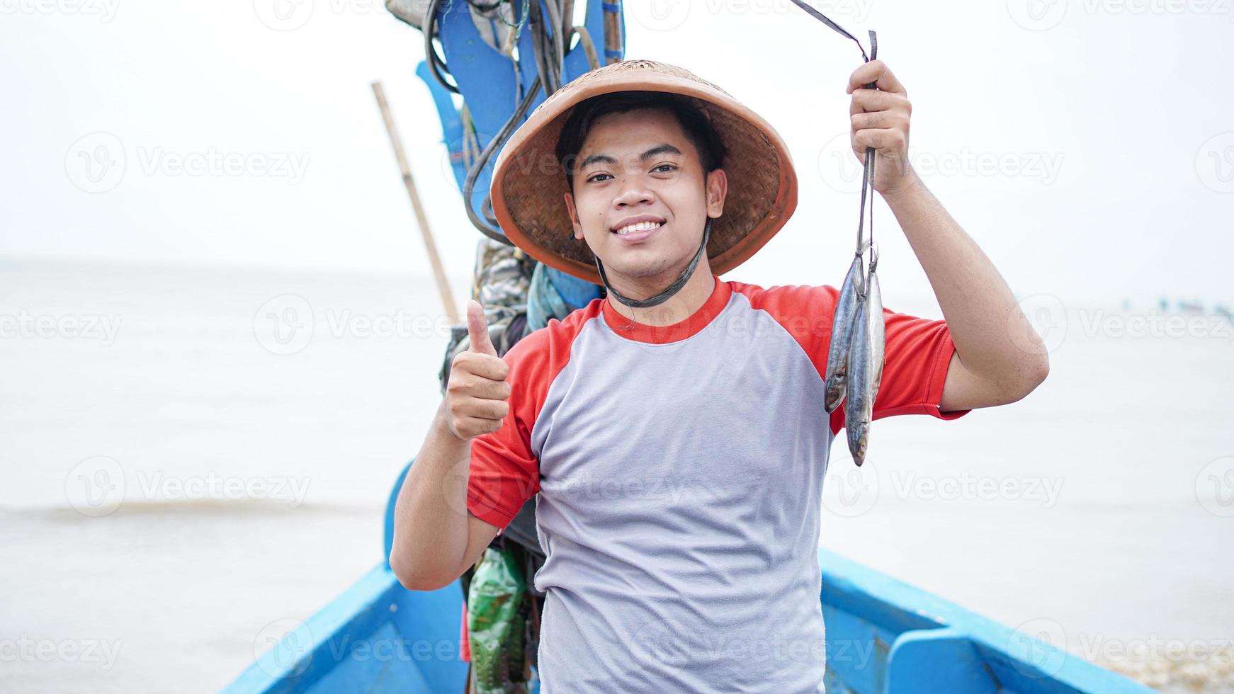 Happy young fisherman on the beach holding his catch fish and shows in front of his boat photo