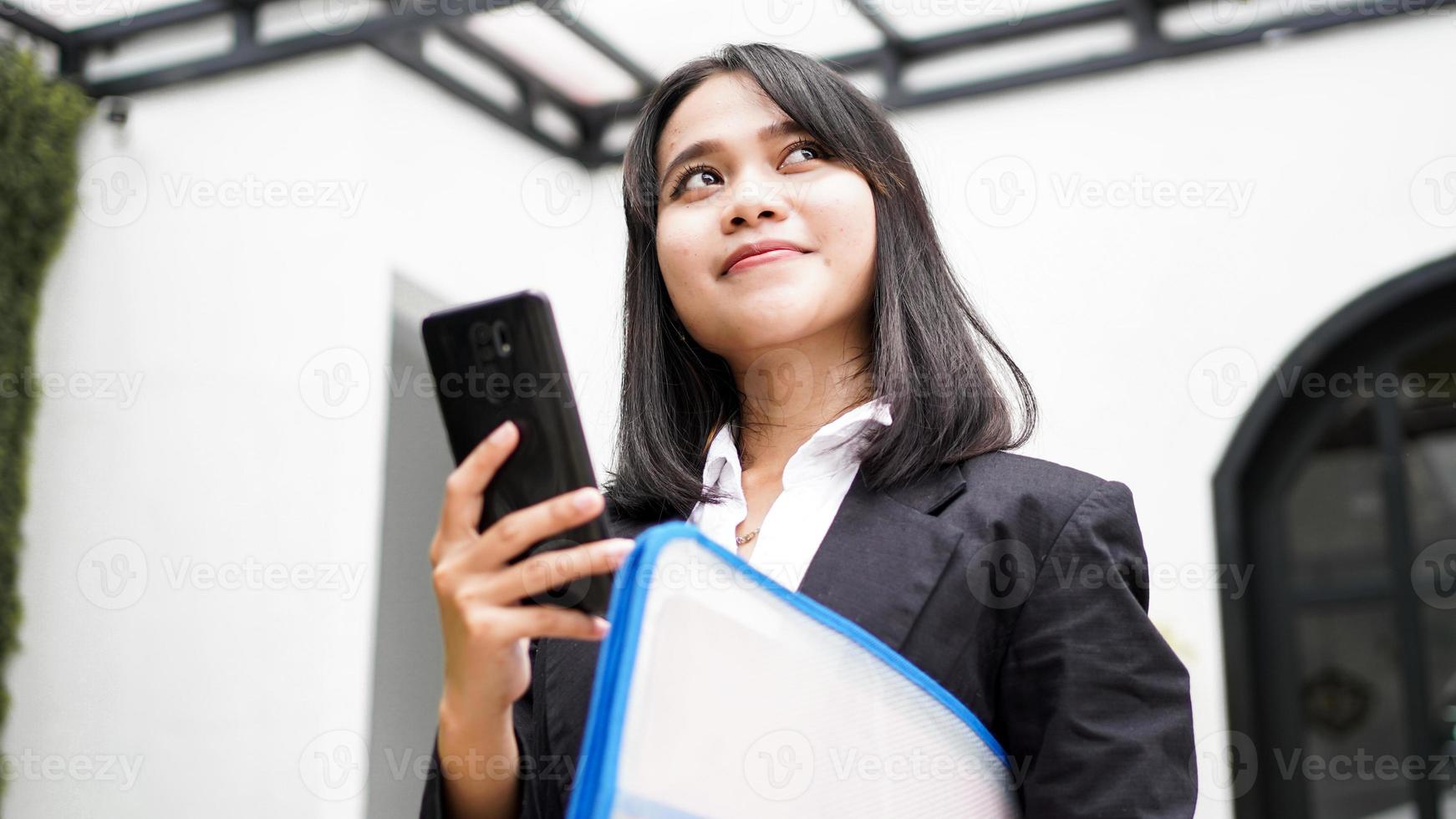 hermosa joven mujer de negocios asiática en traje de pie en el café con teléfono y sobre marrón foto