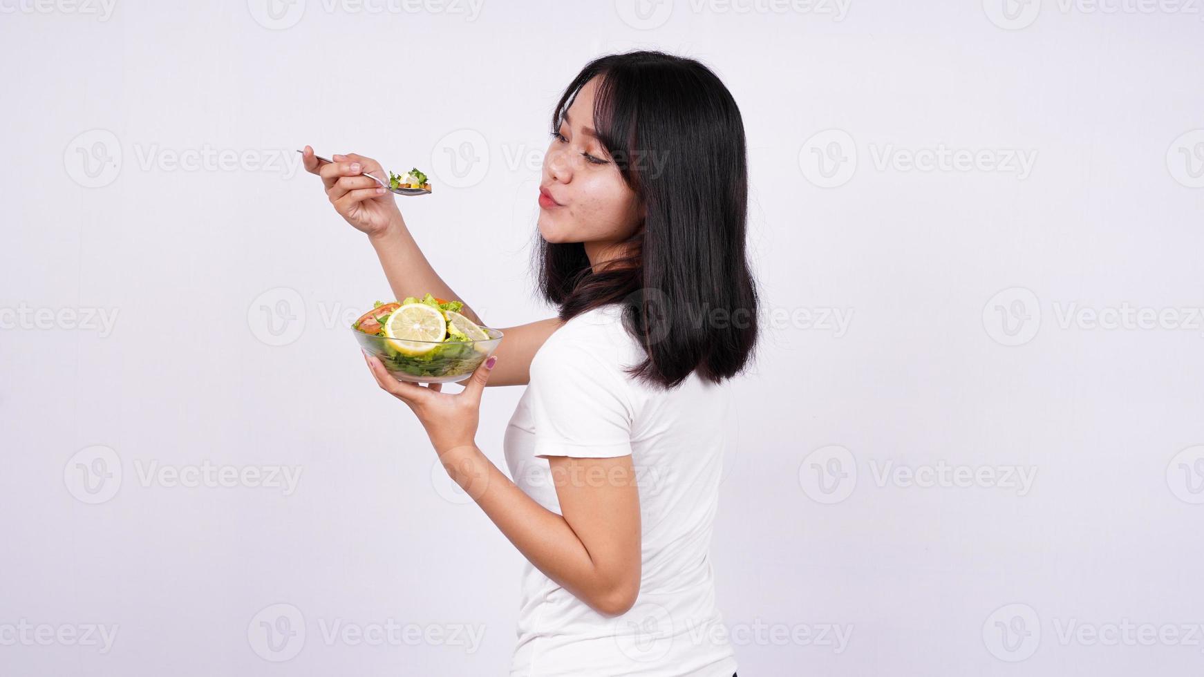 joven mujer asiática feliz comiendo ensalada saludable con fondo blanco aislado foto