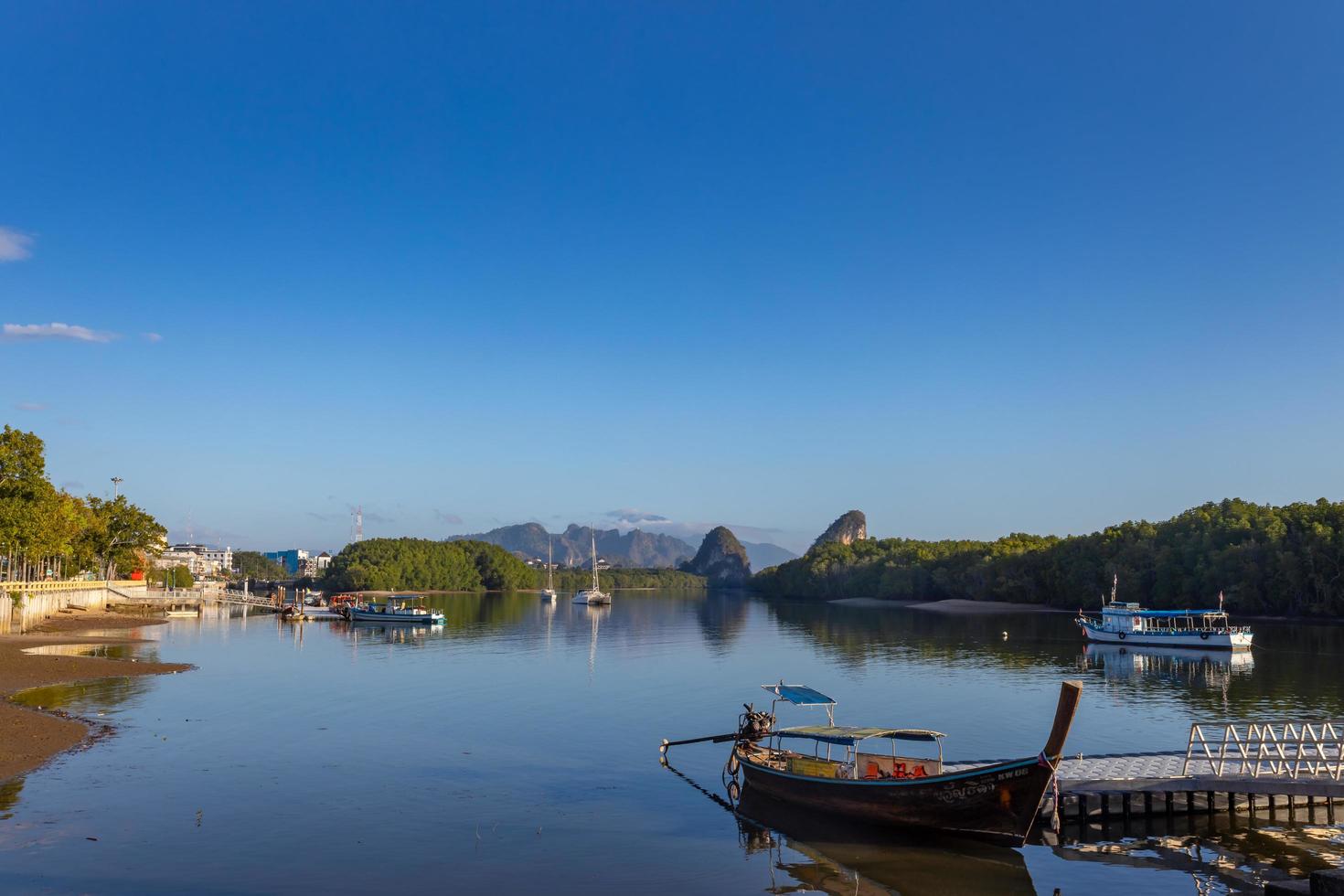 KRABI, THAILAND - JANUARY 23, 2020 - Beautiful natural view of boats, pier, mangrove forest and Khao Khanab Nam mountain at Krabi River, Krabi, Thailand. photo